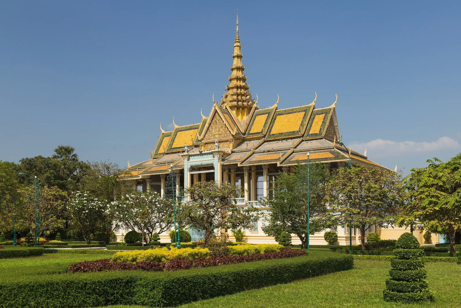 Golden spired pavilion of the Royal Palace rises above manicured gardens in Phnom Penh under a clear blue sky.