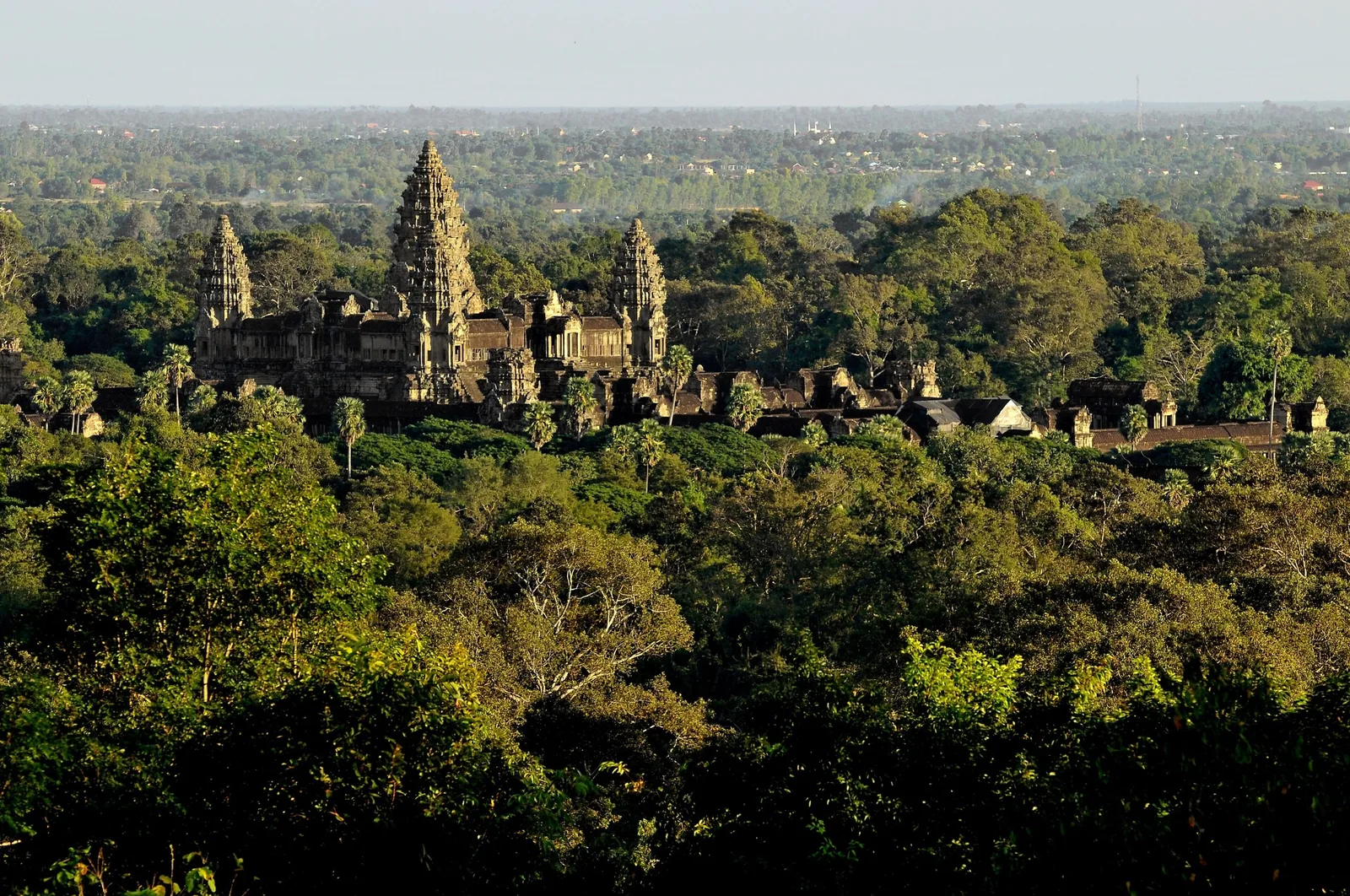 The towering spires of Angkor Wat rise above a dense green forest canopy near Siem Reap.