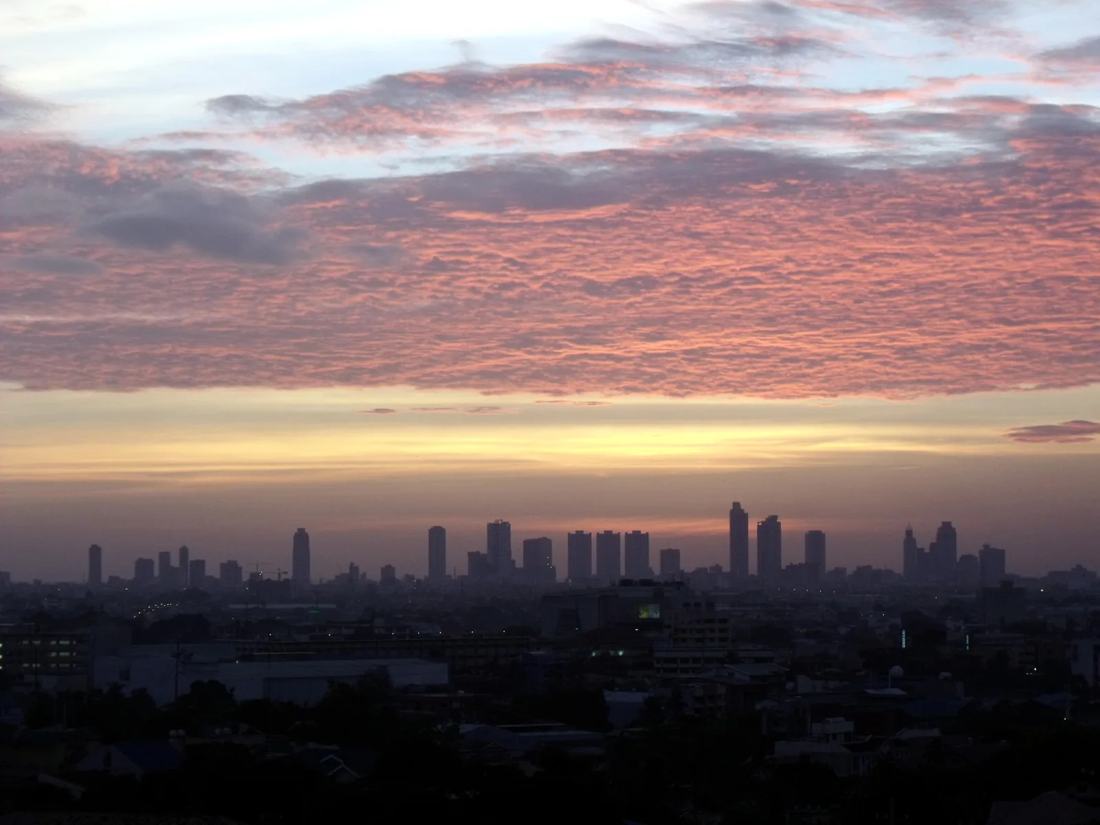 Pink-toned clouds at sunset over the Manila skyline silhouette