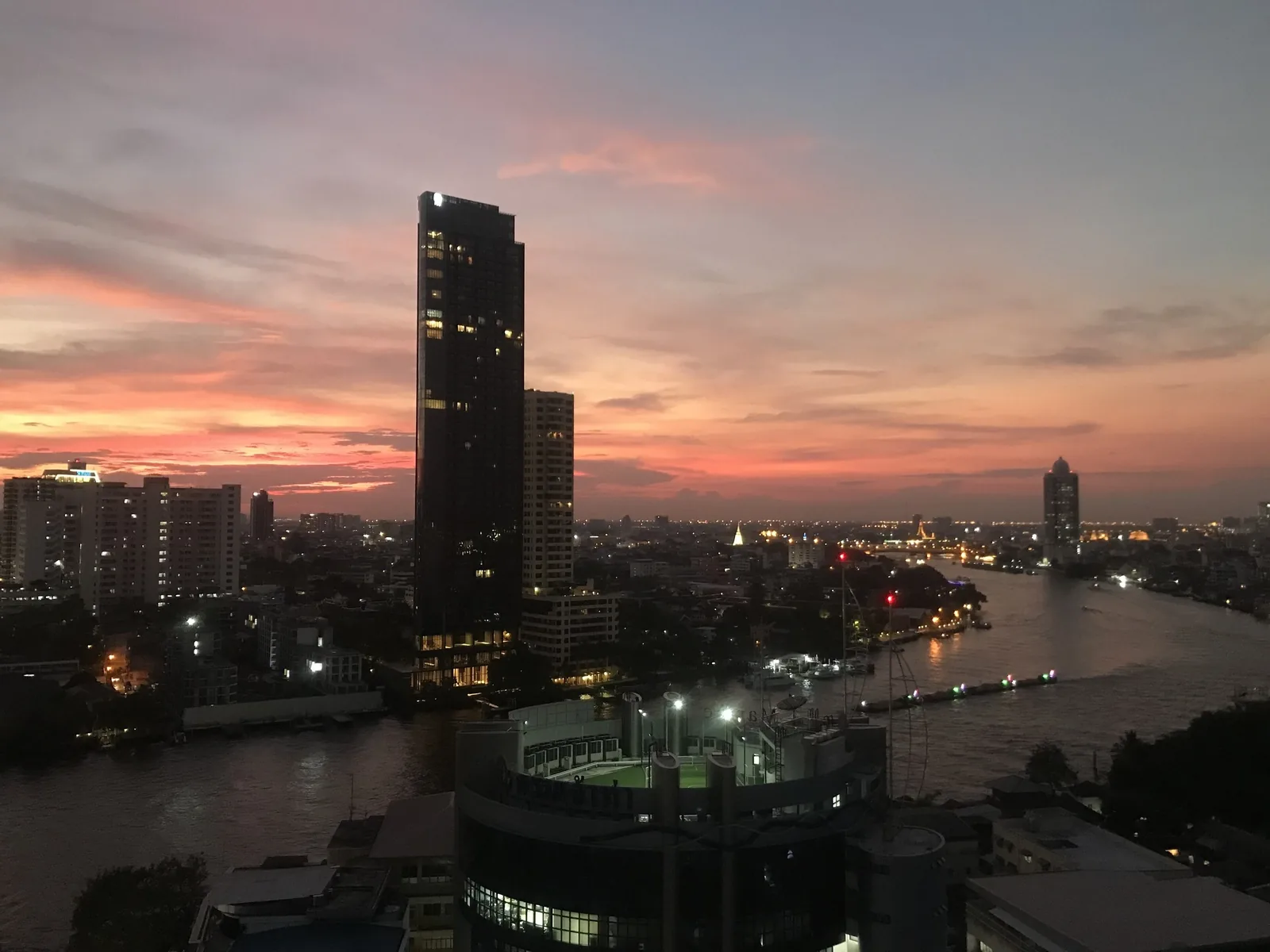 A pink sunset glows over the Chao Phraya River and Bangkok's skyline of high-rise towers.