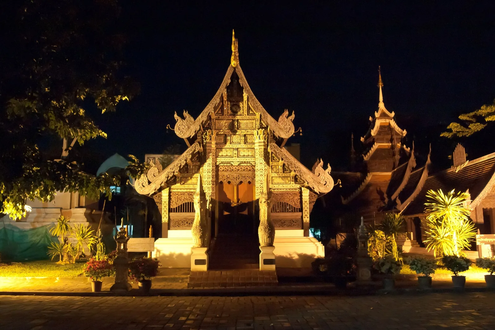 A gilded Thai temple pavilion glows under lights at night in Chiang Mai, Thailand.