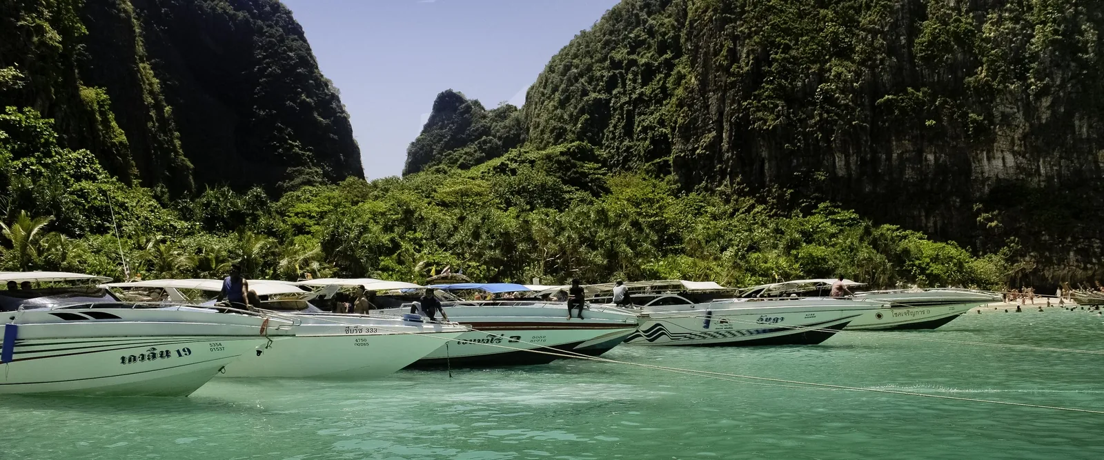 Speedboats moored in the turquoise waters of Maya Bay, surrounded by limestone cliffs near Krabi, Thailand.