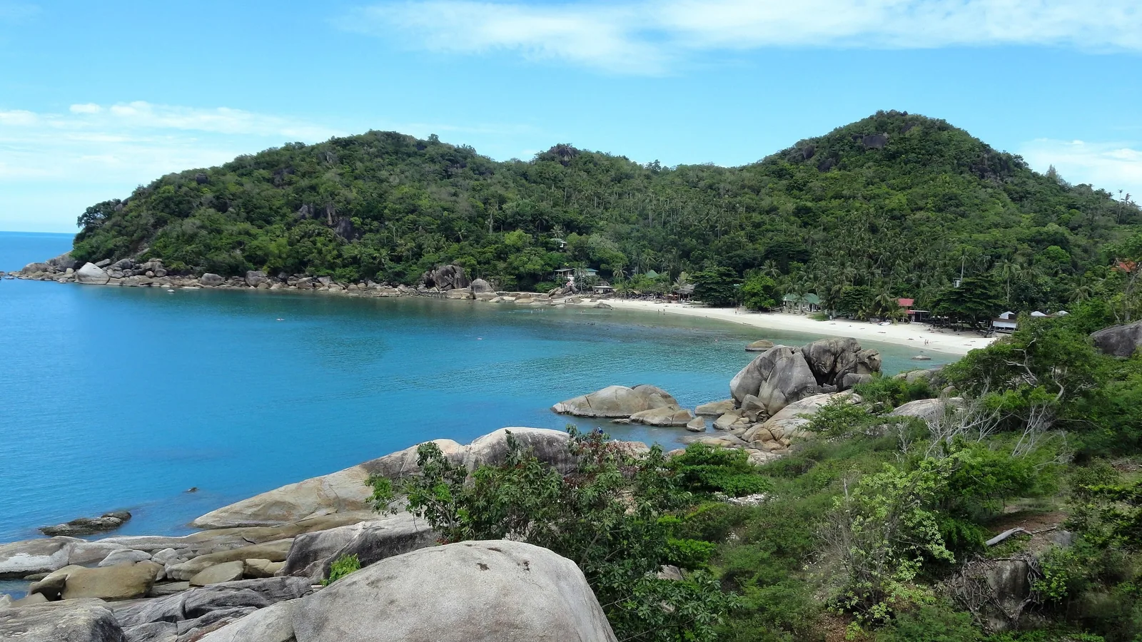 A secluded bay with turquoise water, granite boulders, and a forested headland at Thong Ta Kian Beach, Koh Samui.