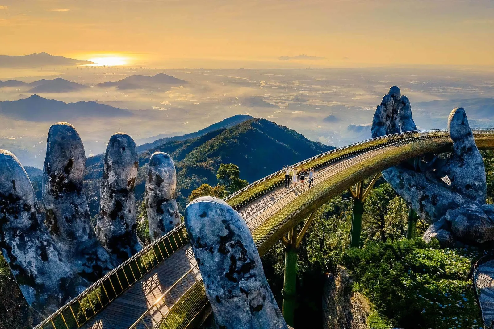 Golden Bridge at Ba Na Hills held by giant stone hands, overlooking misty mountains at sunset