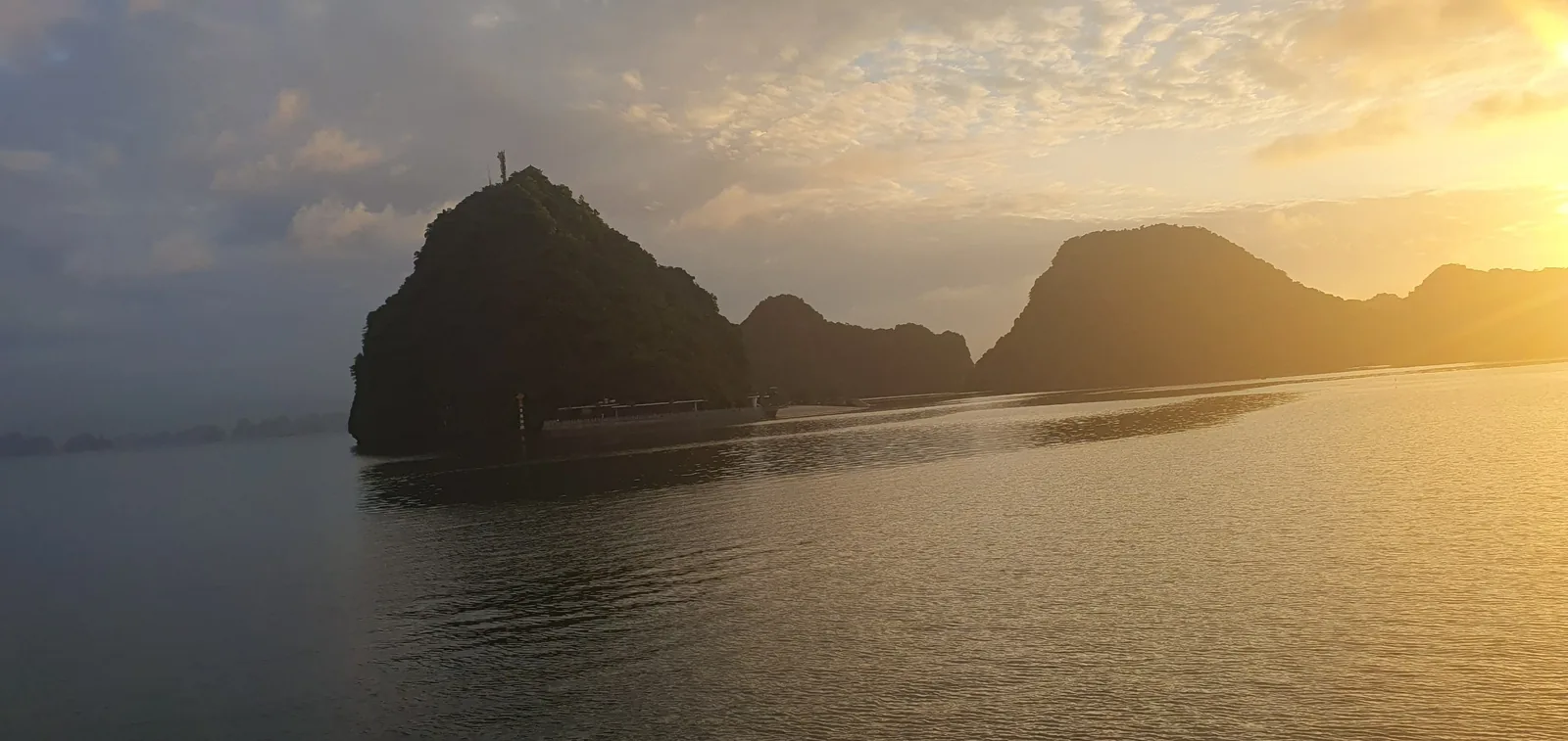 Golden sunset light glows over limestone karst islands rising from the calm waters of Halong Bay.