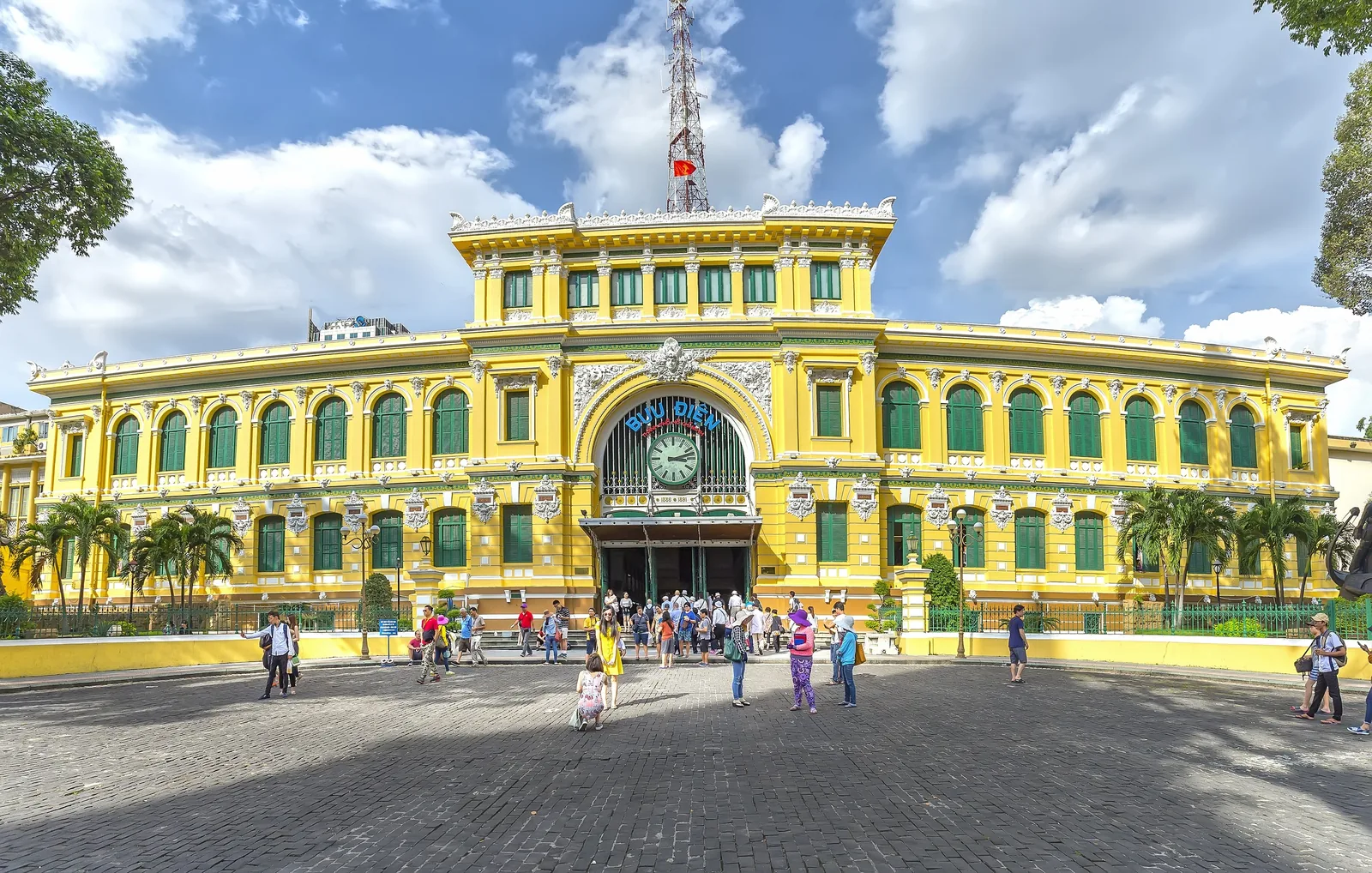 Yellow French colonial facade of Saigon Central Post Office with visitors gathered on the plaza below.
