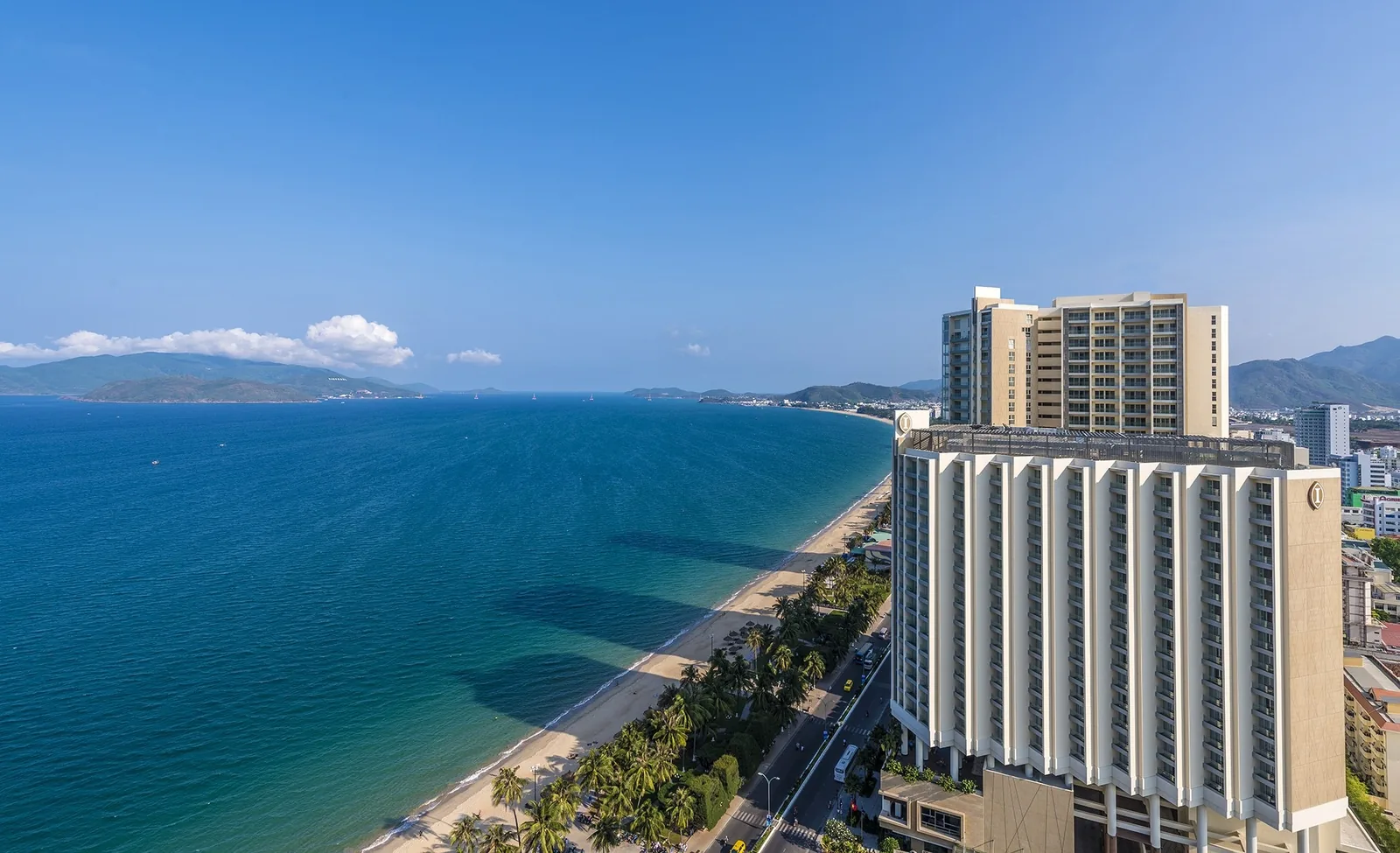 Aerial view of a high-rise beachfront hotel along Nha Trang's curving coastline with turquoise sea and mountains beyond.