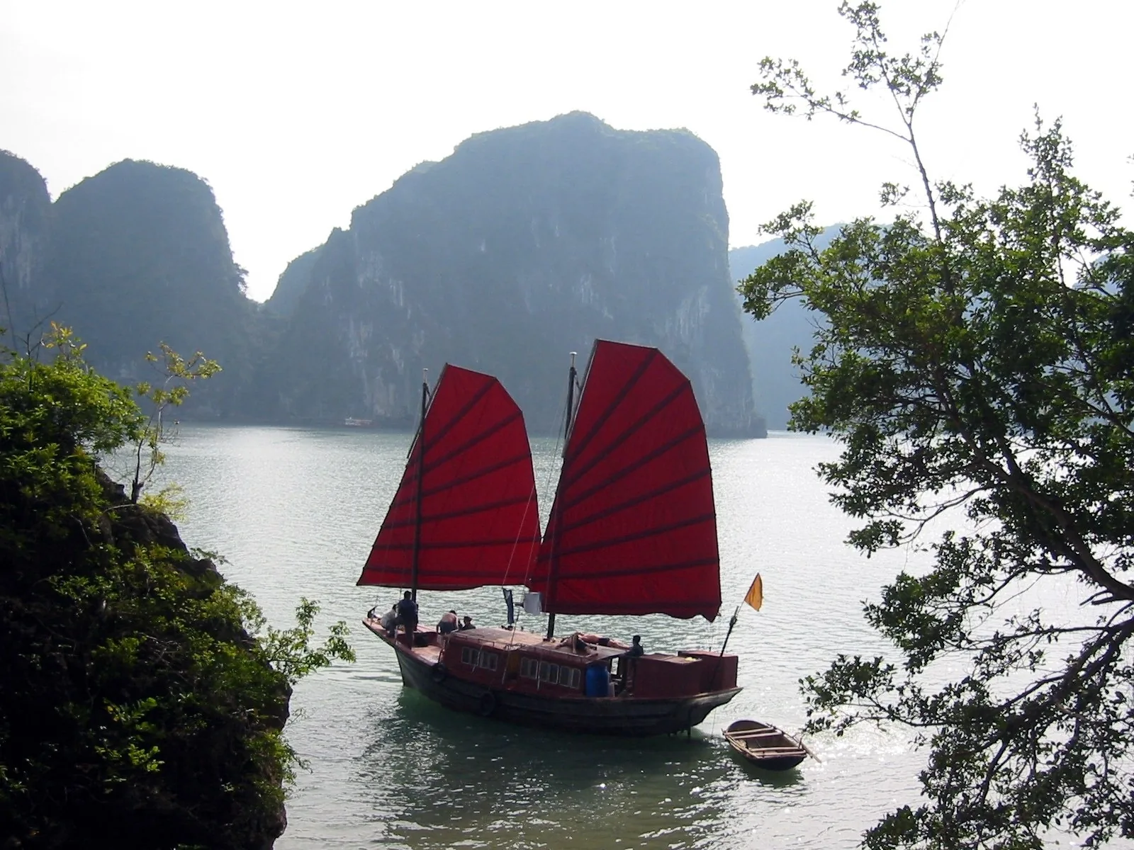 A red-sailed junk boat drifts among limestone karsts in Ha Long Bay, Vietnam.