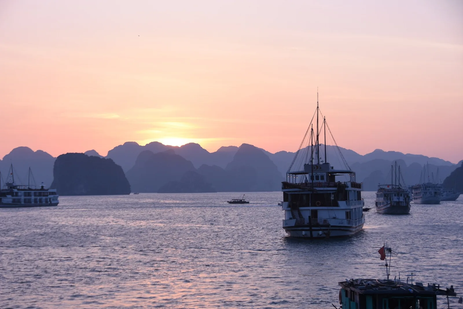 Cruise boats silhouetted against a pink sunset amid limestone karsts in Ha Long Bay