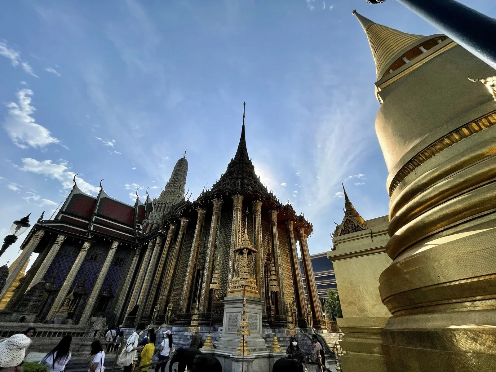 Ornate golden spires of the Temple of the Emerald Buddha rise against a bright sky in Bangkok's Grand Palace complex.