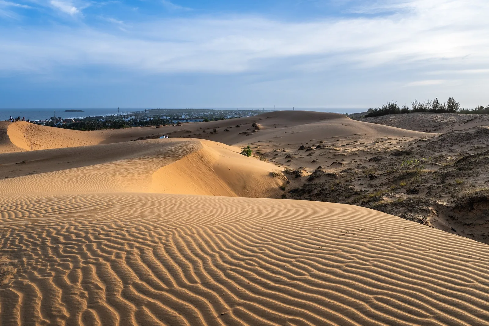 Rippled sand dunes stretch toward the coastal town and sea near Mui Ne, Vietnam.