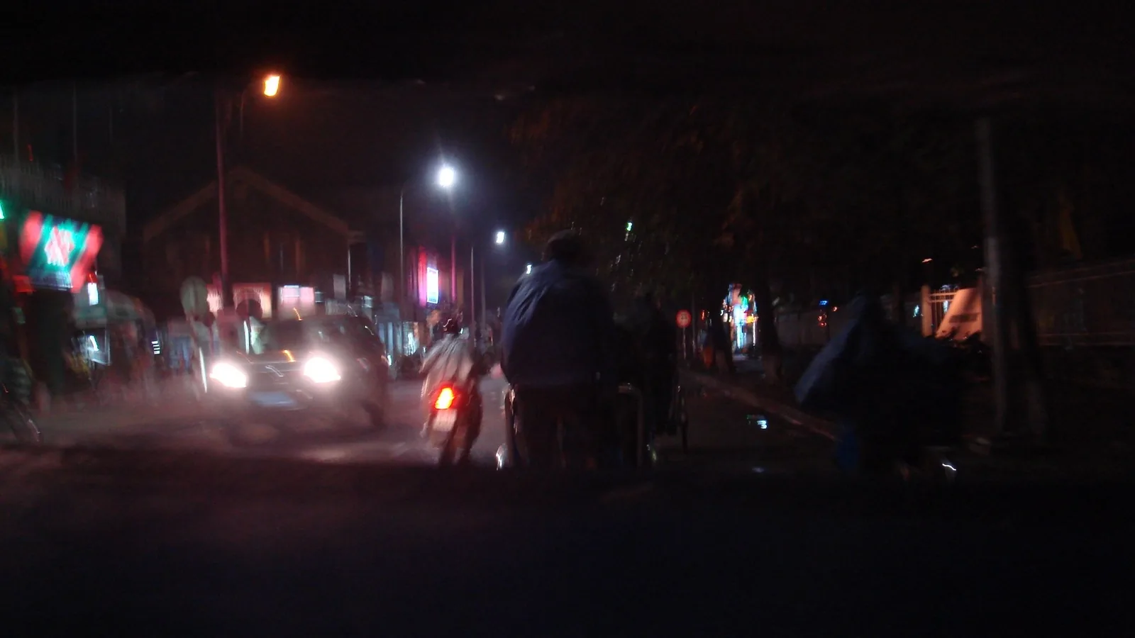 A nighttime street scene in Hue with headlights, streetlights, and pedestrians walking along a dimly lit road.